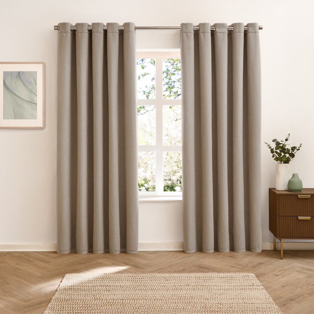 Verso Plain Reversible Eyelet Curtains in mocha hung on a metal pole beside a window, shown in a bedroom with a wooden chest, framed art print, and jute rug.