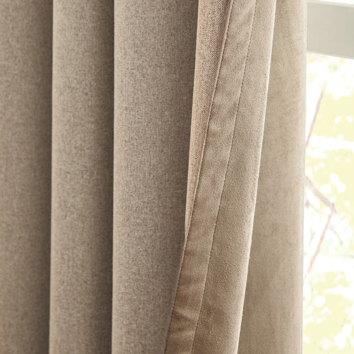 Close-up of Verso Reversible Eyelet Curtains in mocha, showing folded panels with a suede face on one side and a flatter woven reverse, hung by a window.