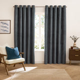 Verso Plain Reversible Eyelet Curtains in petrol blue with a suede-look finish, hung on a metal rail in a living room with an armchair, teal cushion and wooden sideboard.