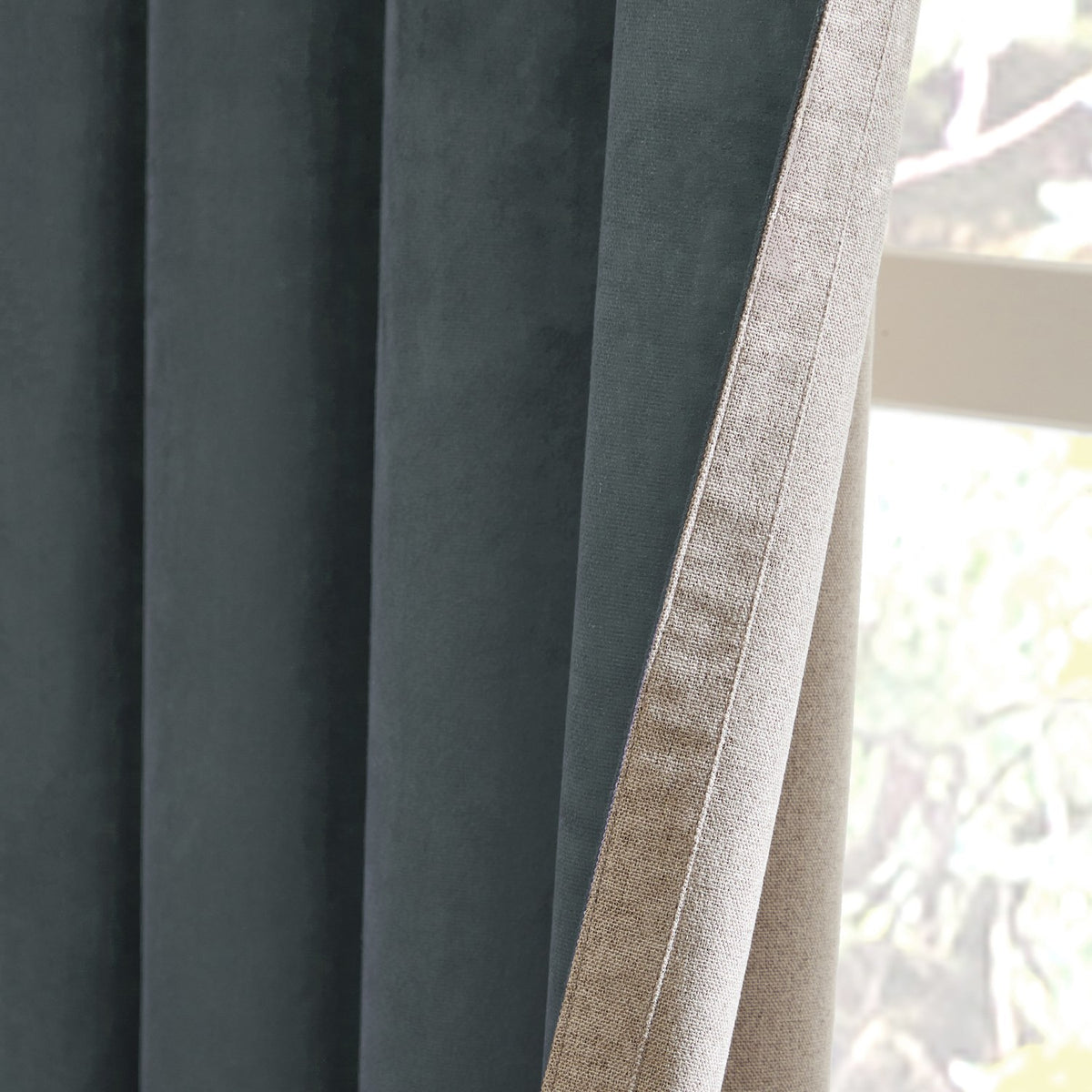 Close-up of Verso reversible eyelet curtain showing petrol blue suede-look face folded back to reveal the natural oatmeal reverse side, with soft pleats near a window.