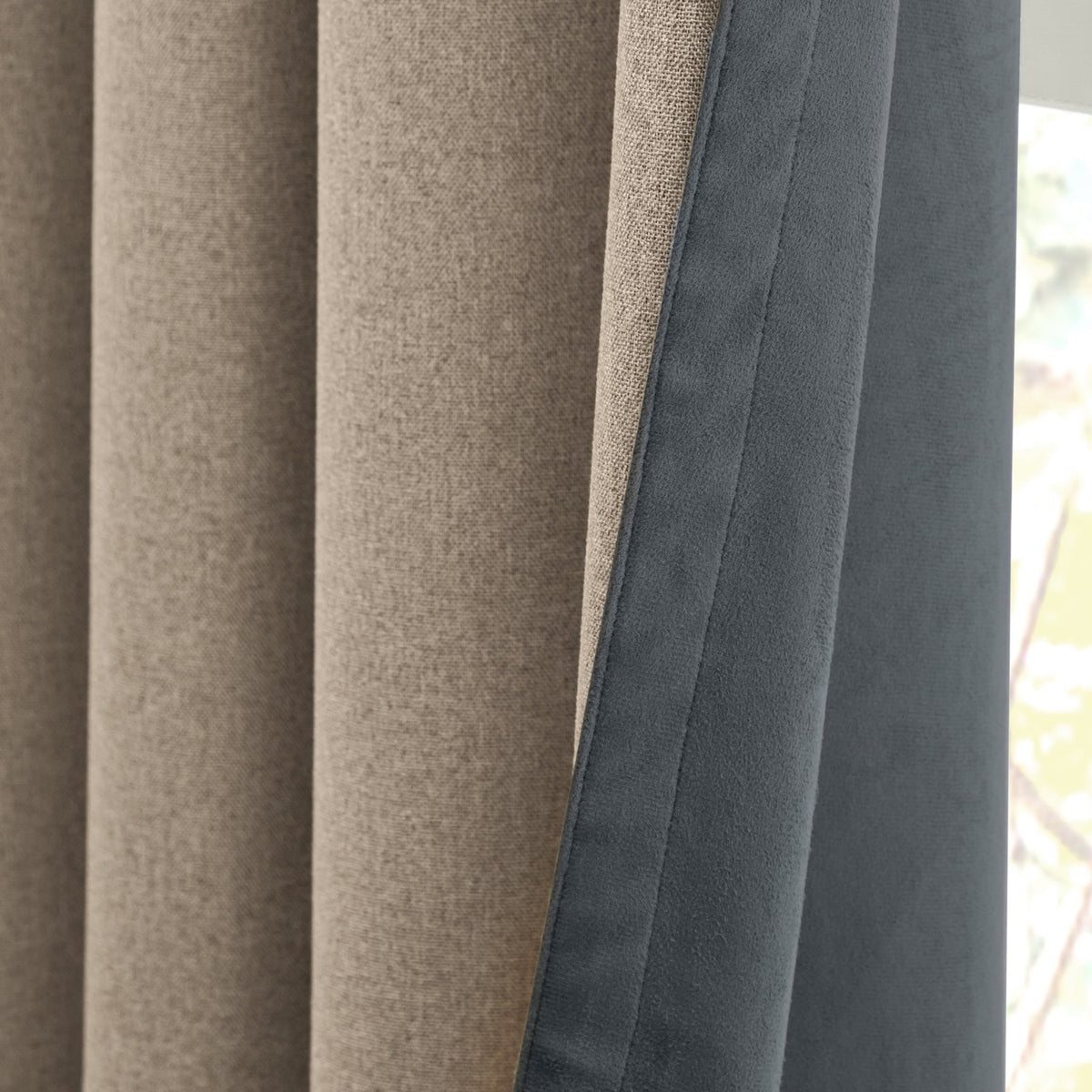 Close-up of Verso reversible eyelet curtain fabric, showing the natural oatmeal woven face folded back to reveal the petrol blue suede-look reverse side.