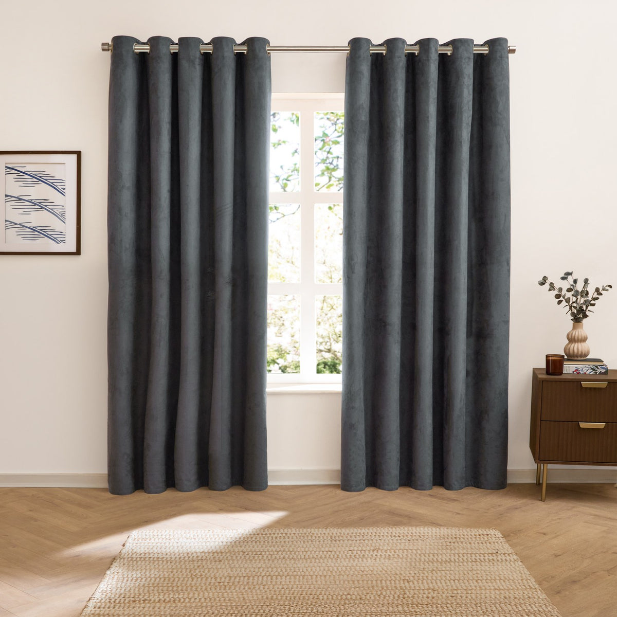 Verso Plain Reversible Eyelet Curtains in petrol blue with a suede-look finish, shown hung on a metal pole in a living room beside a window and wooden cabinet.