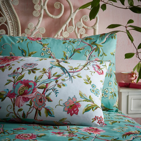 Vintage Chinoiserie Duvet Cover Set in jade with pink floral vines and bird print, shown on a bed with matching pillowcases against a pink wall.