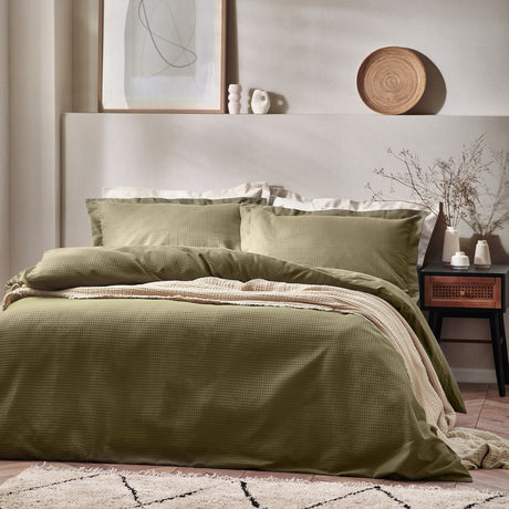 Waffle Cotton Plain Duvet Cover Set in olive green, shown on a bed with matching pillowcases and a striped throw in a neutral Scandinavian-style bedroom.