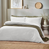 White waffle-textured cotton duvet cover set with matching pillowcases, styled on a bed with olive green throws in a neutral Scandinavian-style bedroom.