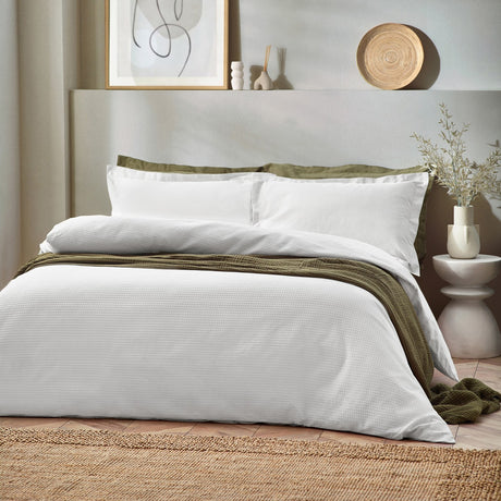 White waffle-textured cotton duvet cover set with matching pillowcases, styled on a bed with olive green throws in a neutral Scandinavian-style bedroom.