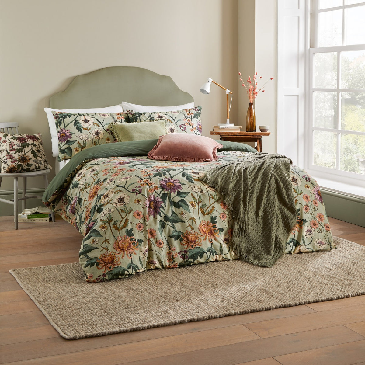 Wallflower Cotton Botanical Duvet Cover Set in celadon green, shown on a bed with matching pillowcases, olive throw and cushions in a bedroom setting.