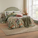 Wallflower Cotton Botanical Duvet Cover Set in celadon green, shown on a bed with matching pillowcases, olive throw and cushions in a bedroom setting.