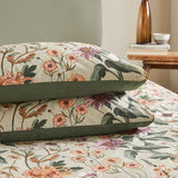 Wallflower Cotton Botanical Duvet Cover Set in Celadon Green, showing pillowcases and duvet with vintage floral print and olive green trim on a bed beside a wooden side table.
