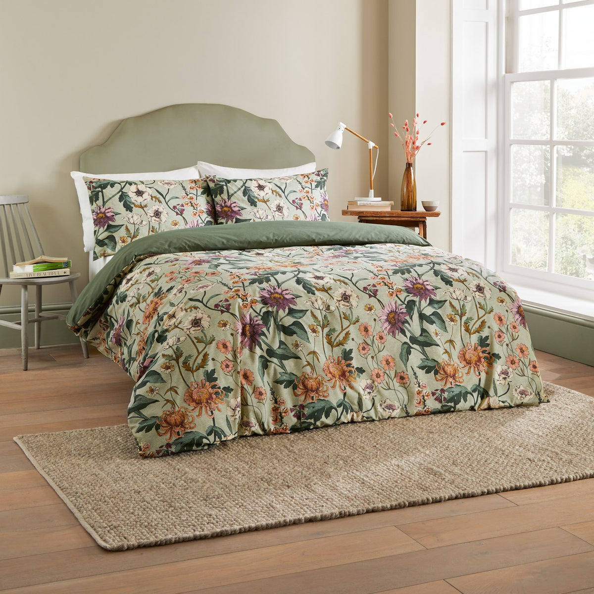 Wallflower Cotton Botanical Duvet Cover Set in Celadon Green on a bed with matching pillowcases and a solid green reverse, styled in a bedroom with wooden headboard and jute rug.