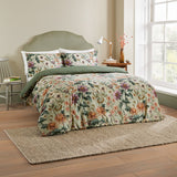 Wallflower Cotton Botanical Duvet Cover Set in Celadon Green on a bed with matching pillowcases and a solid green reverse, styled in a bedroom with wooden headboard and jute rug.