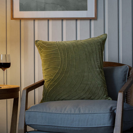 Waterfall Abstract Velvet Cushion in sage green with raised pintuck wave-like ridges, shown on a blue armchair in a living room setting.
