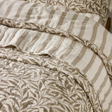 Reversible quilted cotton bedspread in natural, showing the Willow Boughs leaf print folded back to reveal the tonal striped reverse side.