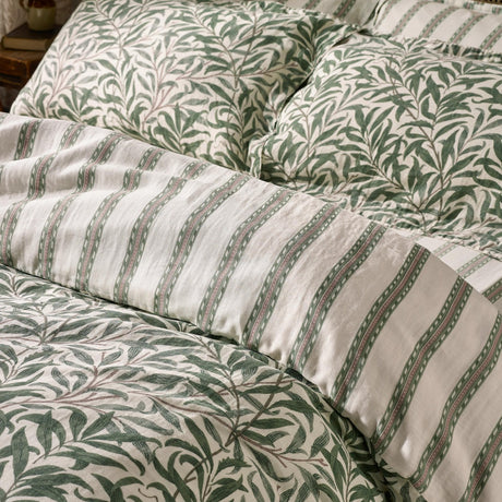Willow Boughs cotton duvet cover set in sage green with a trailing leaf print, shown reversed to its tonal narrow stripe side with matching pillowcases.