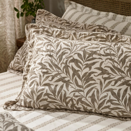 Willow Boughs Reversible Cotton Pillowcase Pair in Natural, showing trailing leaf print pillowcases on a bed with a striped reverse pillowcase and cotton bedding.