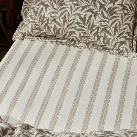 Willow Boughs Percale Cotton Fitted Sheet in Natural, showing a fine vertical stripe with dot detail in soft natural tones on white cotton, styled on a bed with matching leaf-print pillows.