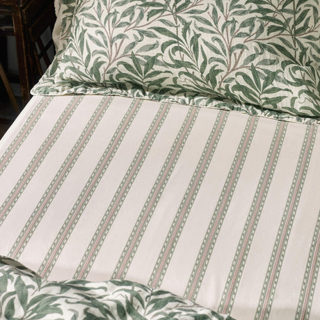 Willow Boughs Percale Cotton Fitted Sheet in Sage, cream ground with fine green and pink striped pattern, shown on a bed with a matching Willow Boughs leaf-print pillowcase.