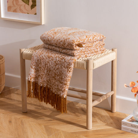 Weaver Geometric Wool Throw in gold, folded with a herringbone weave and tasselled edge draped over a wooden slatted bench in a living room setting.