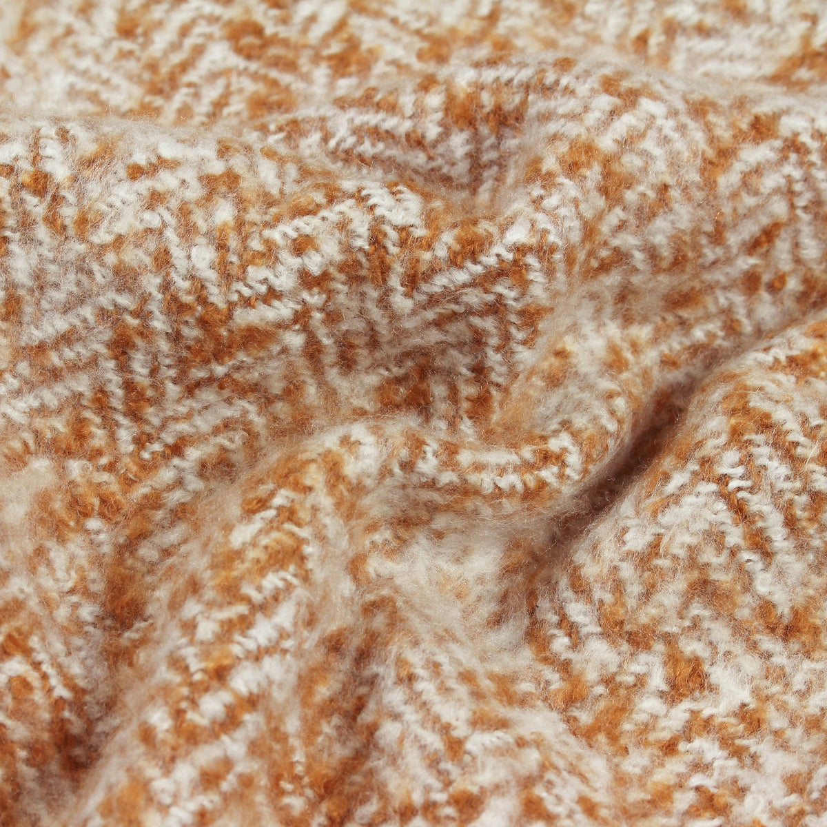 Weaver Geometric Wool Throw in gold, showing a close-up herringbone weave with amber and tan tones over a cream ground, softly draped to reveal its textured fabric.
