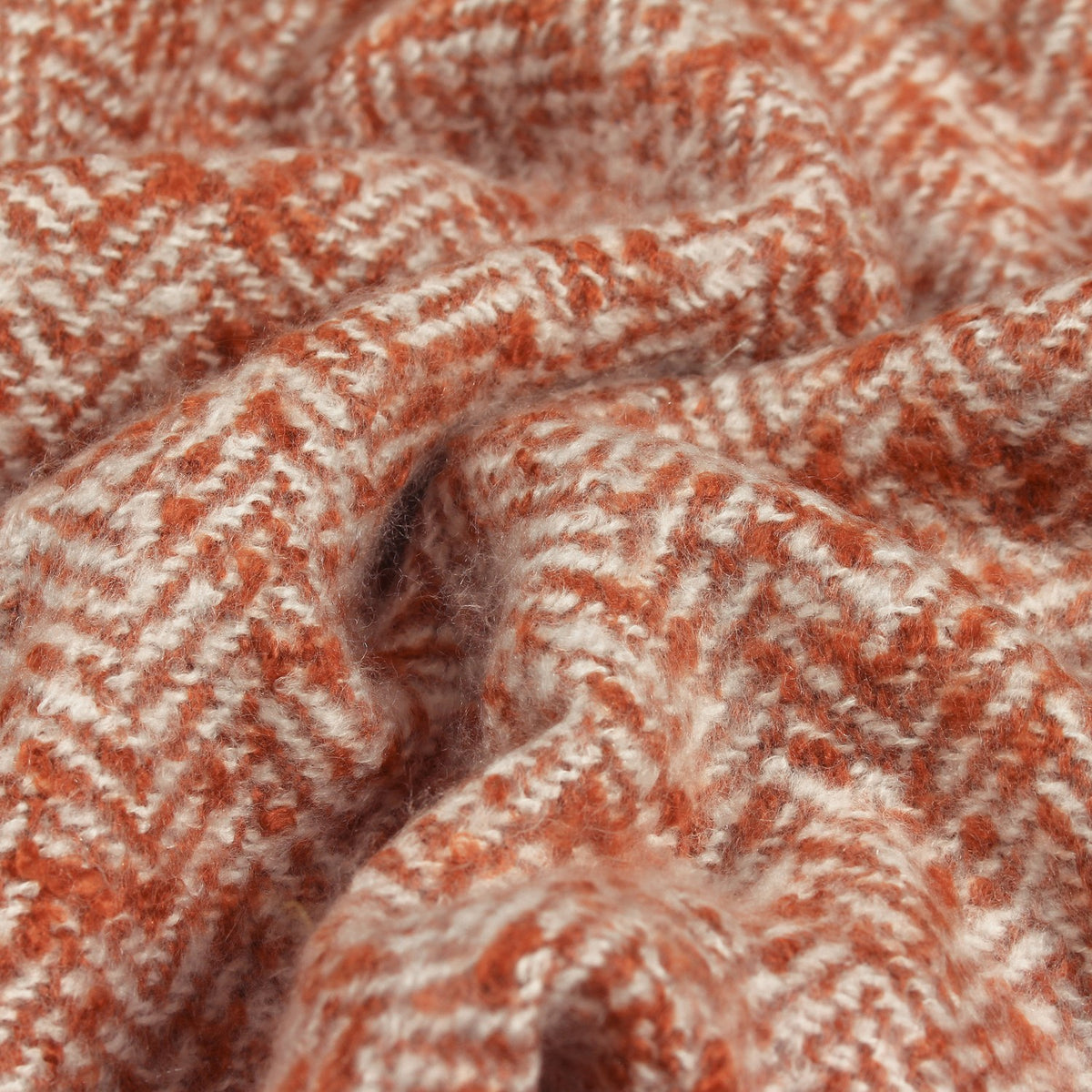 Close-up of the Weaver Geometric Wool Throw in rust, showing a herringbone weave in twisting rust and cream tones with a soft, textured fabric finish.