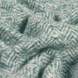 Close-up of the Weaver Geometric Wool Throw in teal, showing a folded herringbone chevron weave in soft teal against a paler ground.