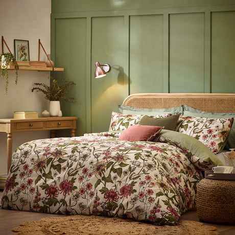 Wallflower Cotton Botanical Duvet Cover Set in Natural styled on a bed with rattan headboard, cream ground floral print, and green and pink cushions in a green-panelled bedroom.