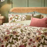Wallflower cotton-blend duvet cover set in natural cream with botanical sunflower, poppy and wildflower print, styled on a bed with green and pink cushions against a rattan headboard.