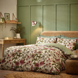 Wallflower Cotton Botanical Duvet Cover Set in Natural, cream cotton-blend bedding with red, gold and green floral print, styled on a bed against a green panelled wall.