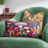 Wild Garden Floral Velvet Cushion in wine-red with mushroom and floral print, styled on a green armchair beside a mustard mushroom-print cushion.