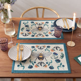 Wild Garden Animal Polyester Placemats with bumblebee and mirrored floral design in cream, teal, blue and orange, styled on a wooden dining table with plates, glassware and candles.