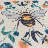 Close-up of a woven polyester placemat with a bumblebee design on a cream ground, surrounded by orange, teal and blue floral motifs and green leaves.