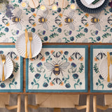 Wild Garden Animal Polyester Placemats with bumblebee and floral motif in cream, teal, orange and blue, teal border, styled on a dining table with matching runner.