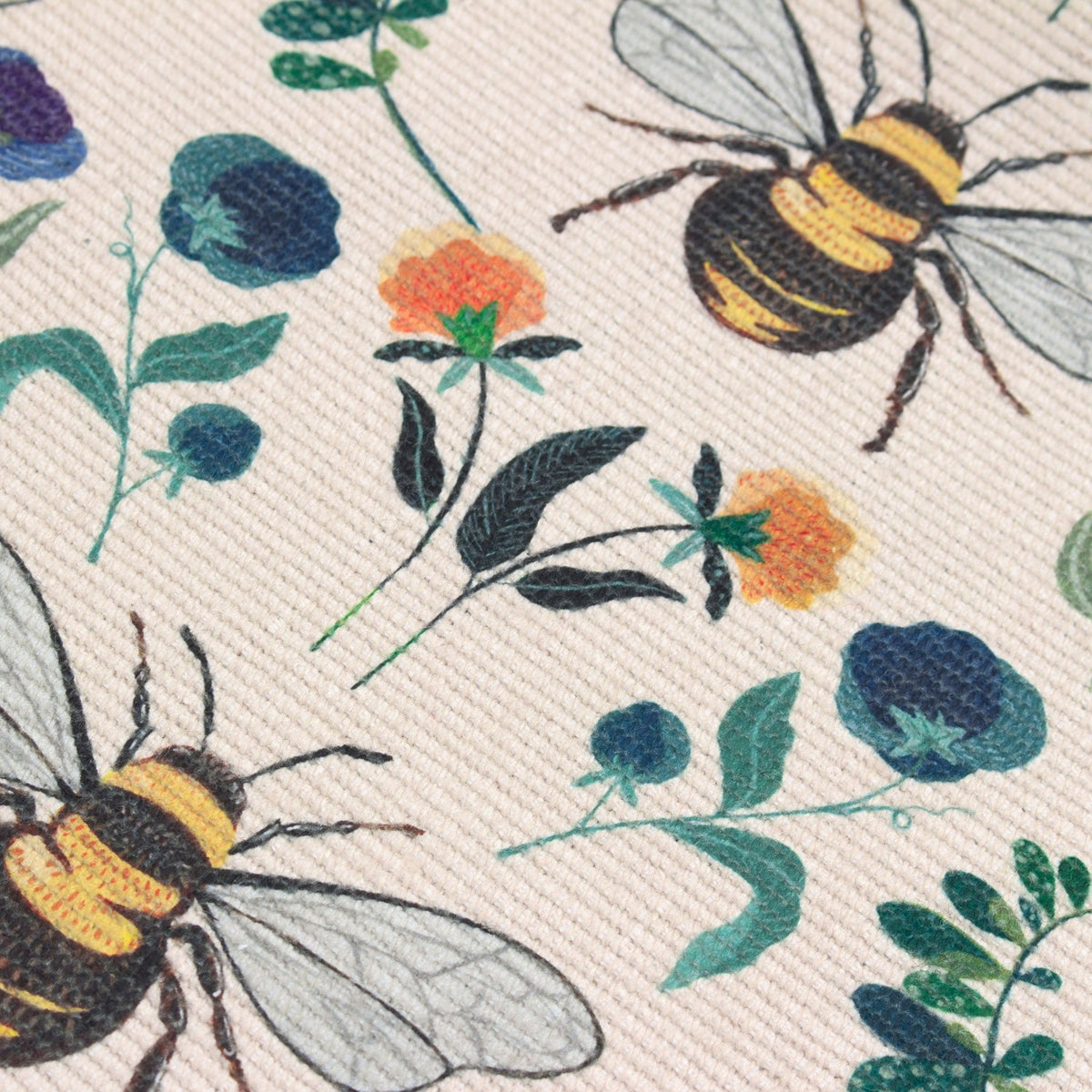 Wild Garden table runner in woven cream polyester, printed with large bumblebees, blue and purple blooms, orange flowers and green foliage.