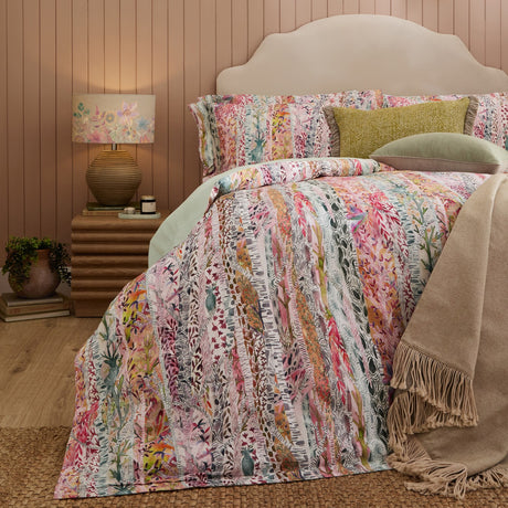 Whimsical Tale cotton sateen duvet cover set in blush, styled on a bed with pillowcases, cushions and a fringed throw in a warm pink bedroom setting.