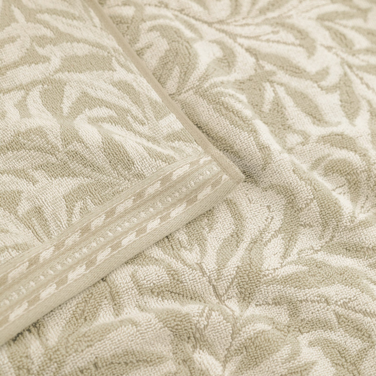 Close-up of the Willow Boughs cotton bath mat in natural, showing sandy beige willow-leaf pattern with a dotted border edge on off-white ground.