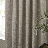 Willow Boughs Jacquard Linen pencil pleat curtains in beige, shown pencil-pleated with a woven trailing leaf pattern, styled near a window with a green plant nearby.