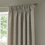 Willow Boughs jacquard linen pencil pleat curtain in beige, shown gathered on a brass pole beside a window, with woven leaf pattern in a neutral room setting.