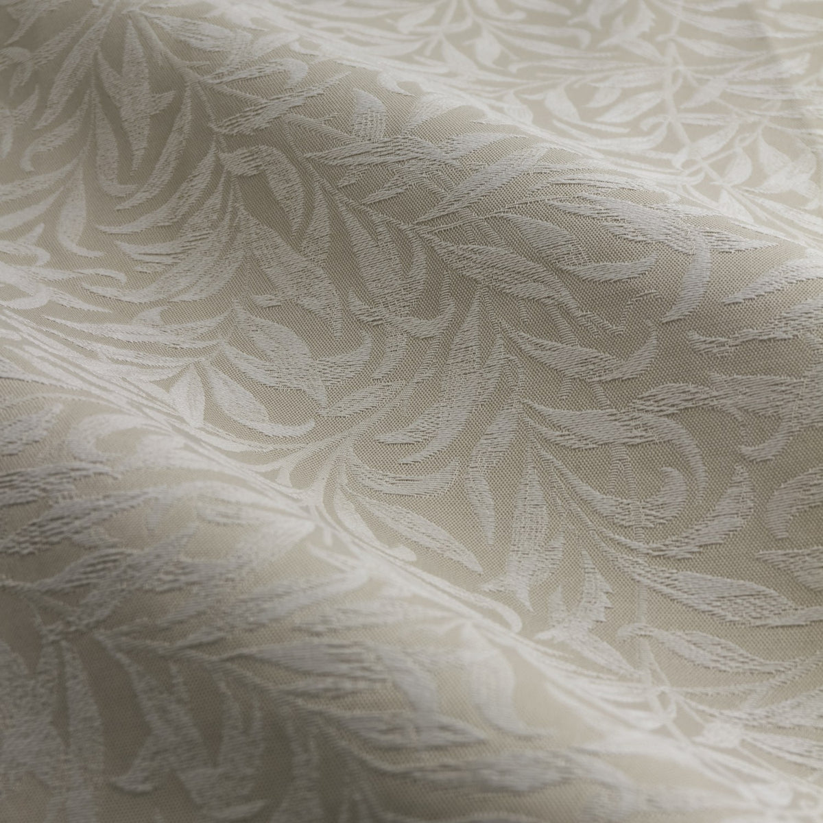 Close-up of Willow Boughs jacquard linen pencil pleat curtain fabric in beige, showing a woven trailing leaf pattern with tonal relief across soft folds.