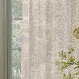 Willow Bough Floral Linen Curtain Panel in cream, a semi-sheer fabric panel with trailing willow leaf print, shown hanging beside a window with pale green frame.