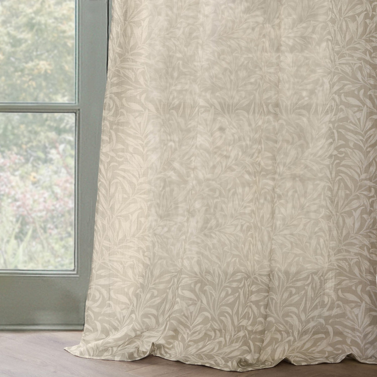 Willow Bough Floral Linen Curtain Panel in cream, a semi-sheer fabric panel with trailing willow leaf print, hanging beside a window with a sage-green frame.