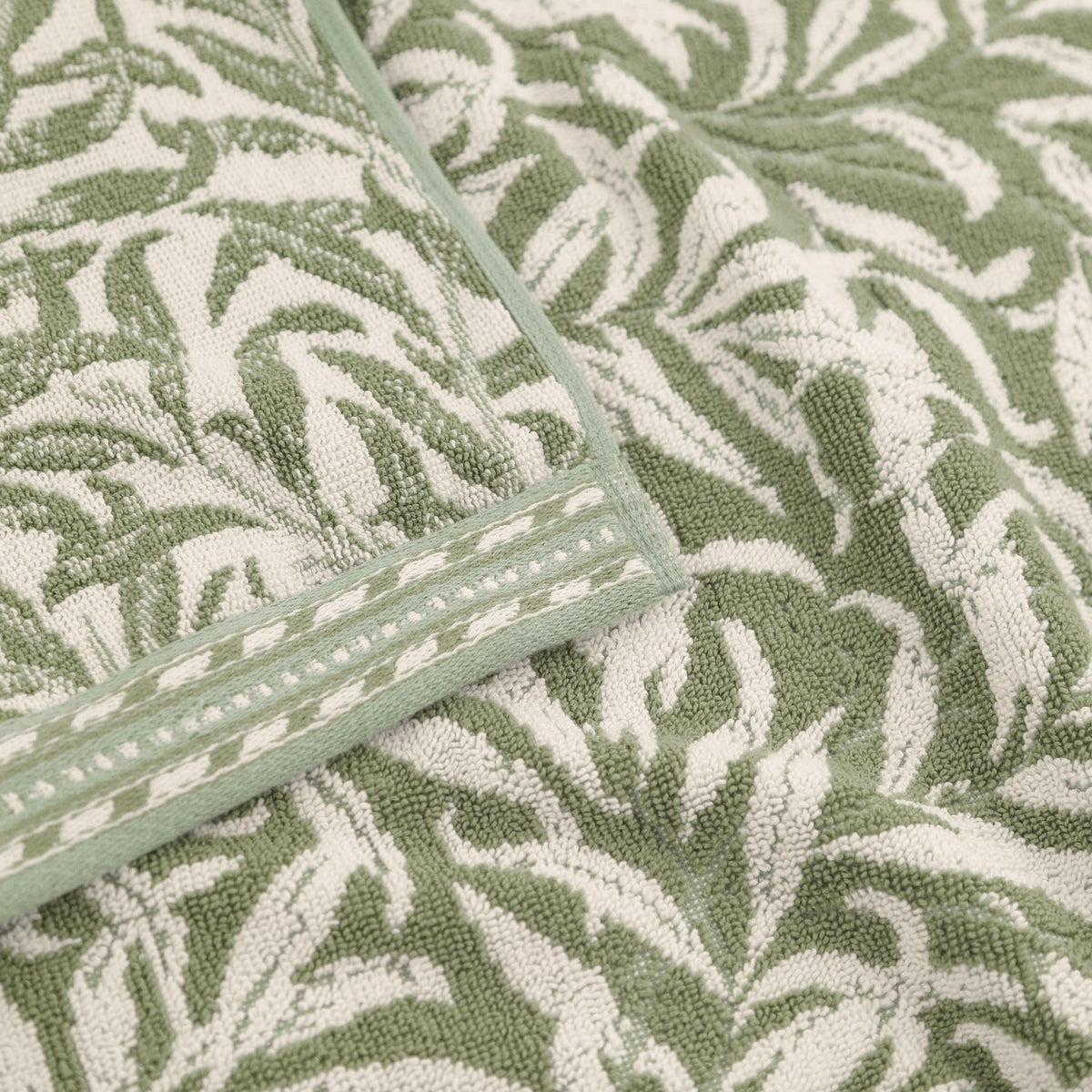 Close-up of Willow Boughs jacquard cotton towels in sage green, showing the woven leaf and stem pattern with a striped woven border trim.