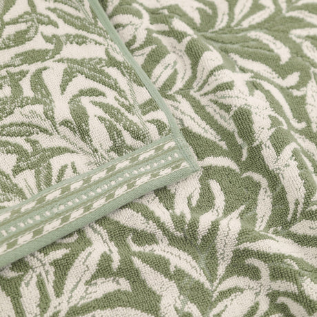 Close-up of Willow Boughs jacquard cotton towels in sage green, showing the woven leaf and stem pattern with a striped woven border trim.