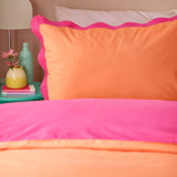 Wiggle Scallop duvet cover set on a bed, showing coral orange and vivid pink cotton-blend fabric with a scalloped pink trim, styled with a matching pillowcase in a bedroom setting.