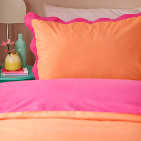 Wiggle Scallop duvet cover set on a bed, showing coral orange and vivid pink cotton-blend fabric with a scalloped pink trim, styled with a matching pillowcase in a bedroom setting.