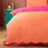 Wiggle Scallop Printed Abstract Duvet Cover Set in coral orange with pink scalloped trim, shown on a bed in a bedroom with a teal side table.