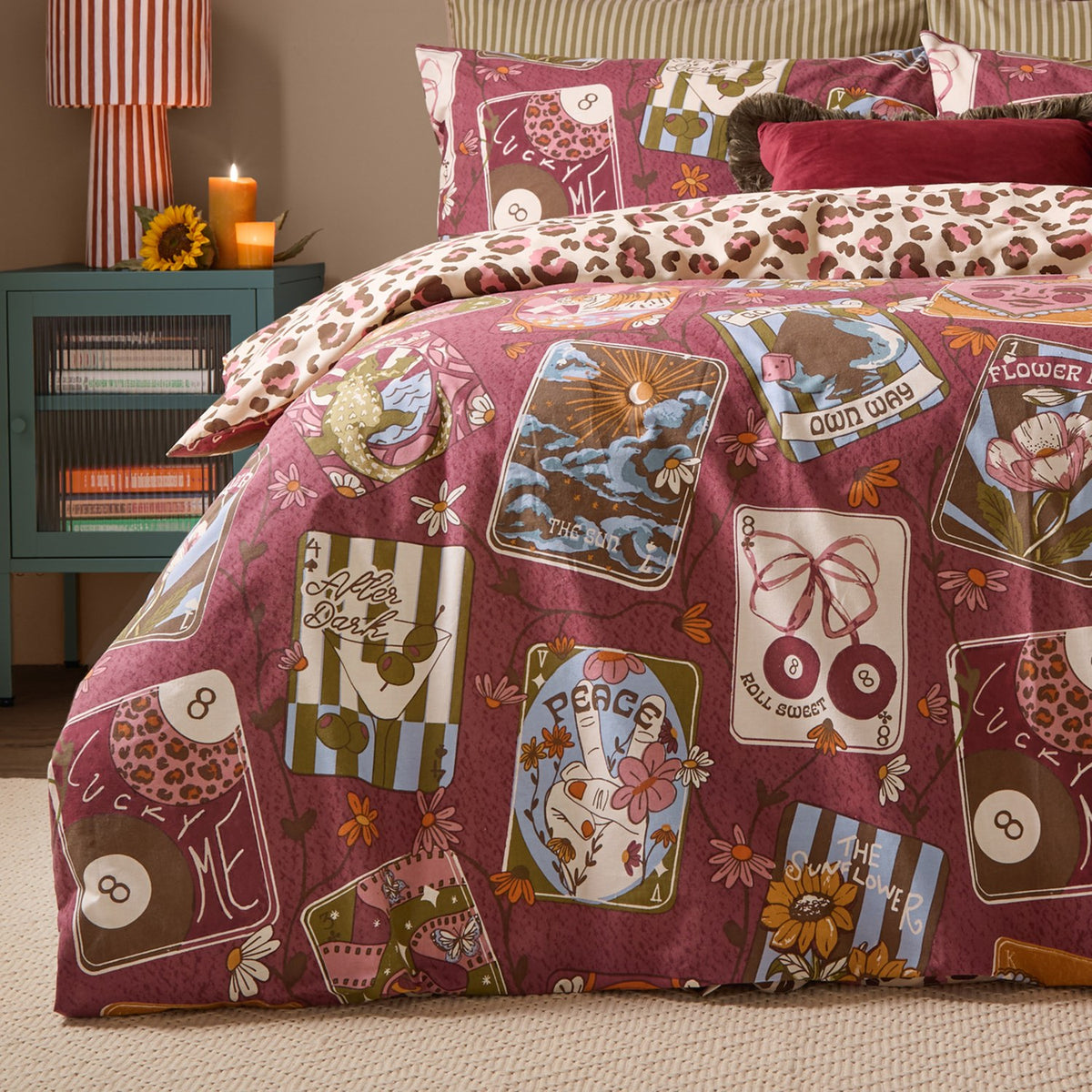 Wild Card Reversible Duvet Cover Set in burgundy, shown on a bedroom bed with tarot-inspired card prints and coordinating leopard-print pillowcases.