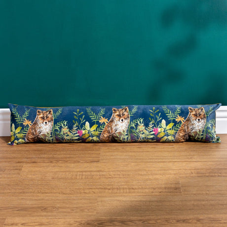 Willow Animal Velvet Draught Excluder in navy, printed with three foxes amid leafy florals, shown on a wooden floor against a teal wall.