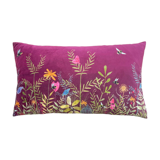 Willow Floral Velvet Cushion in deep fuchsia, rectangular bolster shape with printed meadow design of bees, butterflies and wildflowers in orange, pink and blue, shown on a white background.