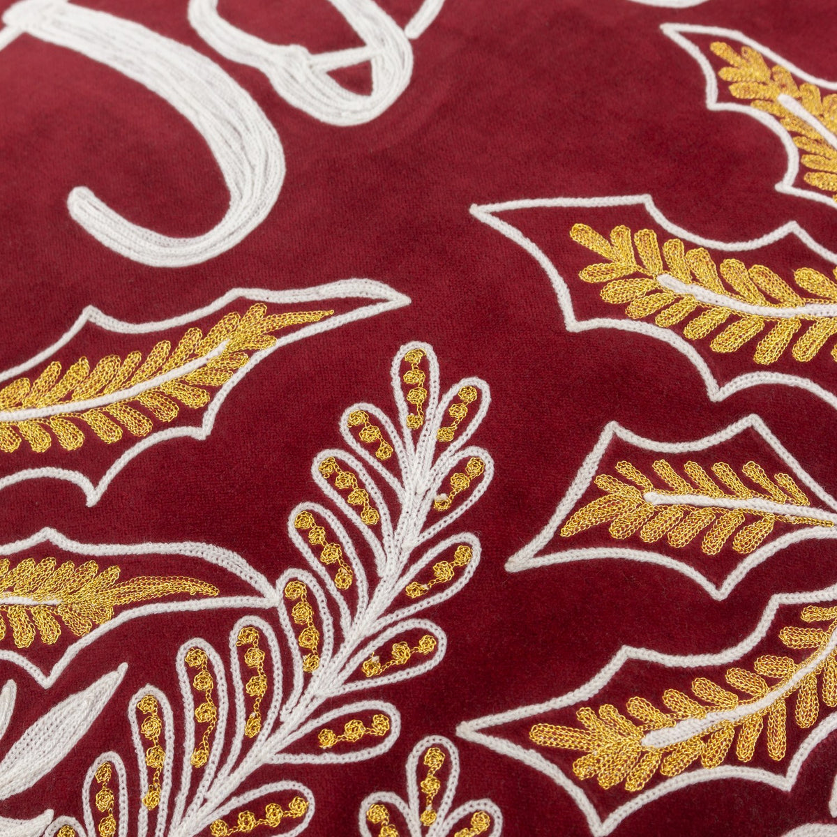 Close-up of the Winter Joy cushion in red cotton velvet, showing gold and white embroidered leaf motifs and part of the hand-lettered "Joy" script.