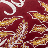 Close-up of the Winter Joy cushion in red cotton velvet, showing gold and white embroidered leaf motifs and part of the hand-lettered "Joy" script.